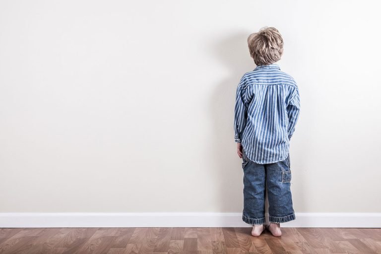 a boy is standing facing the wall during a timeout