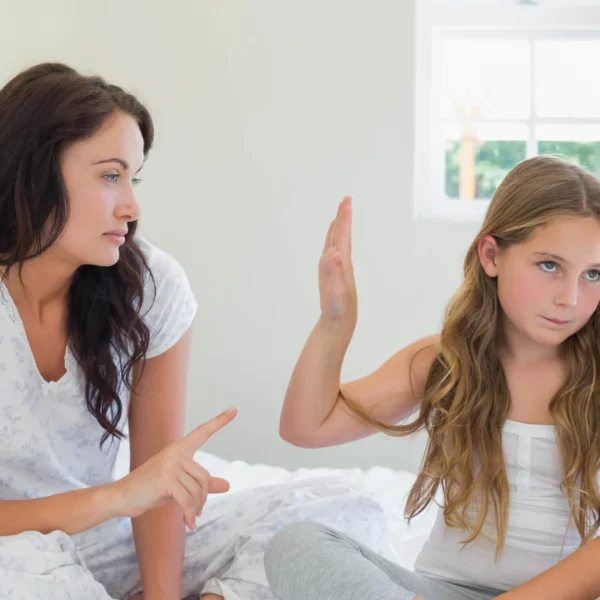 a girl holding up her palm toward her mother, signaling her to be quiet