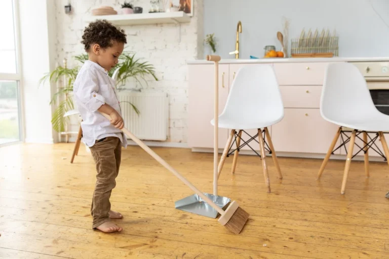 Young child sweeping wooden floor in living room.