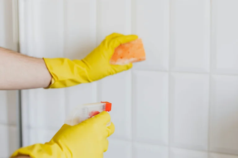 Woman wearing gloves, scrubbing the walls of a bathroom