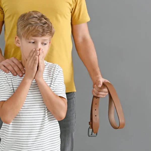 a scared boy covering his mouth as he stares at his father’s belt